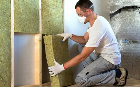 Un ouvrier installe un isolant minéral dans un mur. Pour une isolation par injection, le prix peut varier.