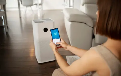 Une femme contrôle son climatiseur Proline via une application sur son smartphone, affichant 58% d'humidité intérieure.