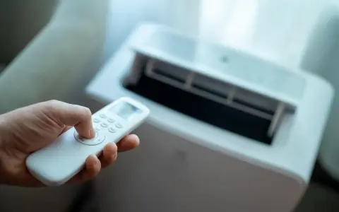 Main tenant utilise la télécommande pour régler son meilleur climatiseur mobile pas cher.