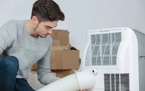 Un jeune homme installe un climatiseur mobile 40m2. Des cartons sont empilés derrière lui.