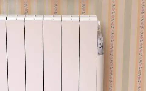 Un radiateur électrique à inertie blanc, avec son thermostat discret, se tient près d'un mur aux rayures pastel et fleuries.
