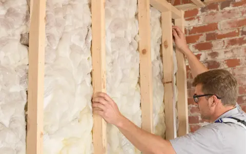 Un ouvrier ajuste la structure en bois d'un mur, révélant une épaisse couche d'isolation intérieure en mousse expansée.
