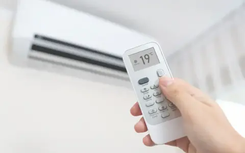 Main tenant ajuste la climatisation chaud à 19°C avec une télécommande.