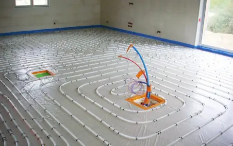 Installation de tubes pour un chauffage électrique au sol. Le sol est recouvert d'une bâche et les tubes blancs sont disposés en spirale.