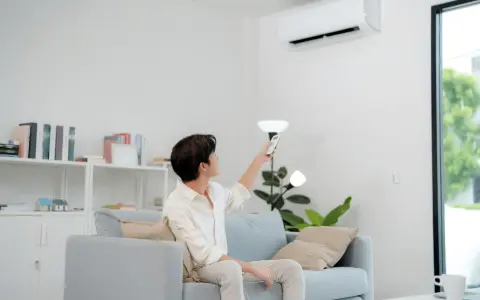 Un homme règle sa télécommande clim Toshiba en mode chauffage depuis son canapé.