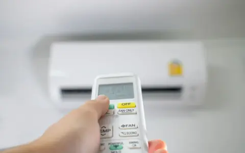 Main tenant utilise la télécommande pour régler la clim en été. La température est affichée sur l'écran.