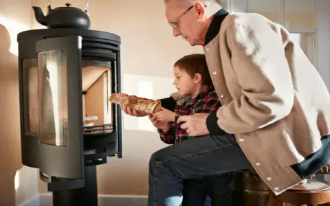 Un grand-père aide son petit-fils à charger du bois dans un poêle. Une alternative au chauffage au fioul, mais attention aux dangers du feu.