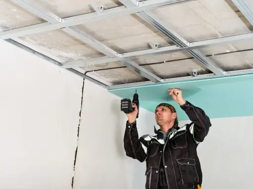 Un ouvrier installe des plaques de plâtre pour l'isolation du plafond de son garage.