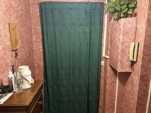 Rideau vert devant une porte, une idée pour comment isoler une porte. Meuble en bois, téléphone, plante verte.