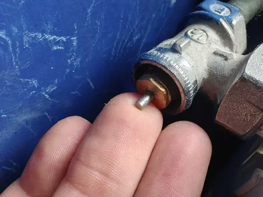 Main d'un doigt touchant la tige d'un robinet thermostatique bloqué chaud, avec une partie métallique visible.