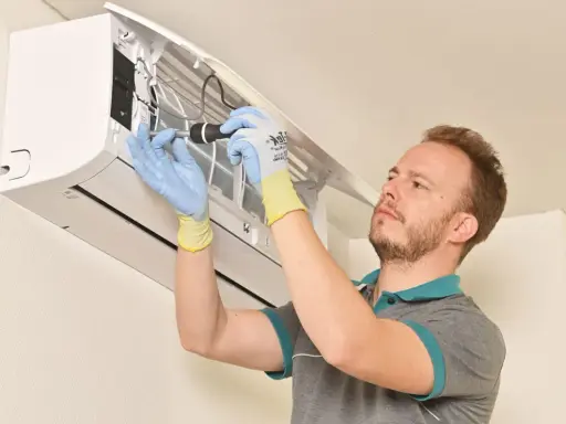 Technicien en gants bleus et jaunes effectuant la mise en service d'une clim split, outil à la main.