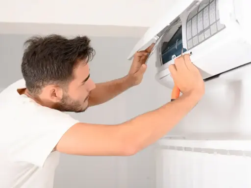 Un homme nettoie une clim avec un tournevis. Il ouvre le capot pour accéder aux filtres.