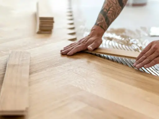 Pose de lames de parquet en bois, créant un motif en chevrons. L'isolation du sol est assurée par la colle appliquée.