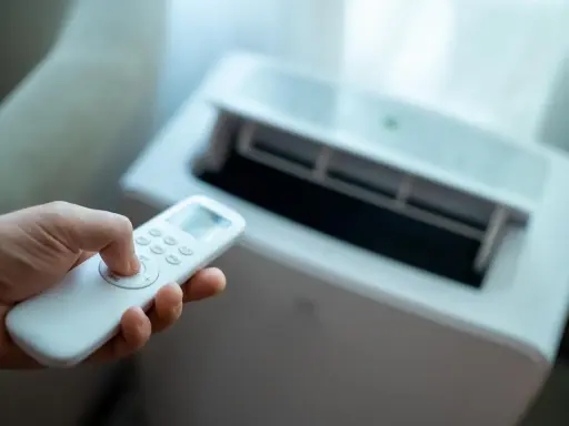 Main tenant utilise la télécommande pour régler son meilleur climatiseur mobile pas cher.