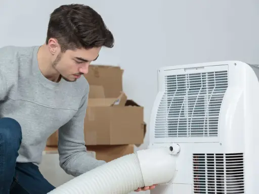 Un jeune homme installe un climatiseur mobile 40m2. Des cartons sont empilés derrière lui.