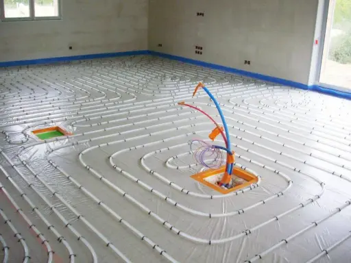 Installation de tubes pour un chauffage électrique au sol. Le sol est recouvert d'une bâche et les tubes blancs sont disposés en spirale.