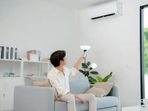 Un homme règle sa télécommande clim Toshiba en mode chauffage depuis son canapé.