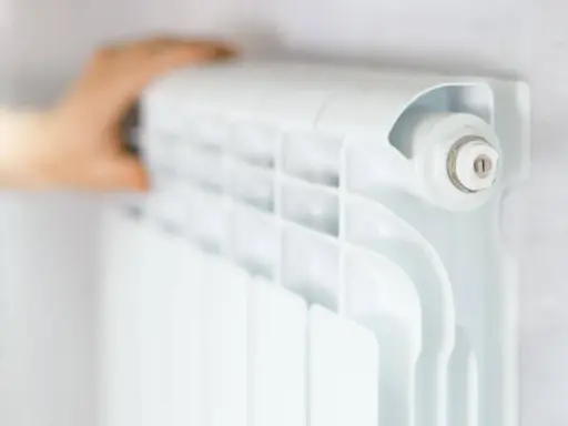 Main d'une personne ajustant un radiateur blanc, élément clé du système chauffage maison.