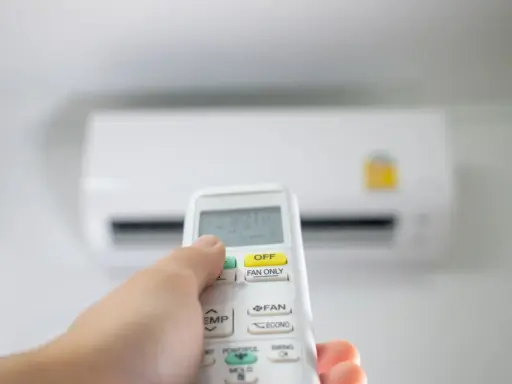 Main tenant utilise la télécommande pour régler la clim en été. La température est affichée sur l'écran.