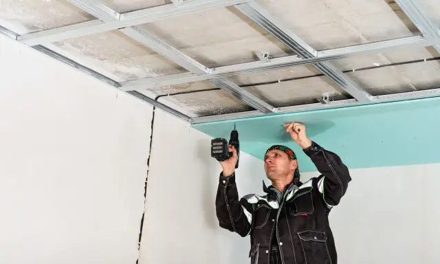 Un ouvrier installe des plaques de plâtre pour l'isolation du plafond de son garage.