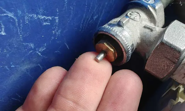 Main d'un doigt touchant la tige d'un robinet thermostatique bloqué chaud, avec une partie métallique visible.