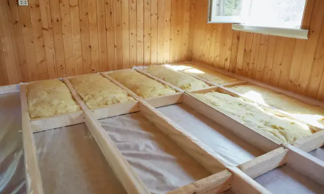 Travaux d'isolation plancher bois en cours. Laine de verre posée entre les solives en bois, prête pour la prochaine étape de construction.