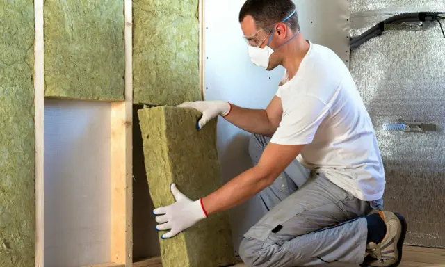 Un ouvrier installe un isolant minéral dans un mur. Pour une isolation par injection, le prix peut varier.