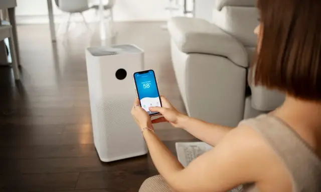 Une femme contrôle son climatiseur Proline via une application sur son smartphone, affichant 58% d'humidité intérieure.
