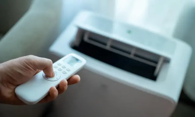 Main tenant utilise la télécommande pour régler son meilleur climatiseur mobile pas cher.