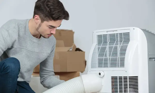 Un jeune homme installe un climatiseur mobile 40m2. Des cartons sont empilés derrière lui.