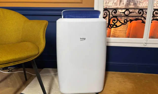 Climatiseur Beko, blanc, avec une sortie d'air bleue. Un fauteuil moutarde et une vue sur des toits parisiens. Avis positifs attendus.