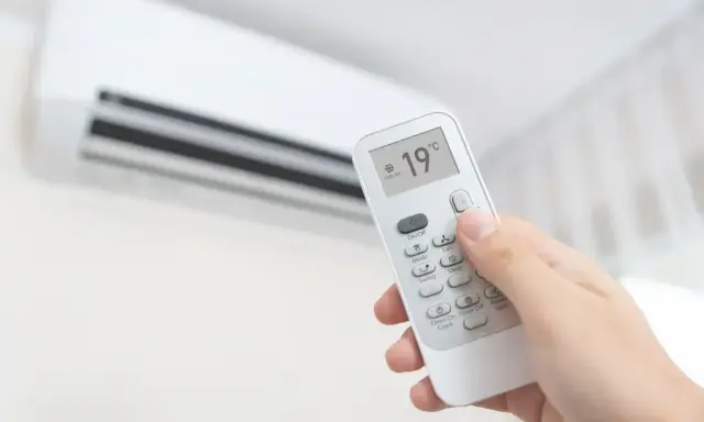 Main tenant ajuste la climatisation chaud à 19°C avec une télécommande.