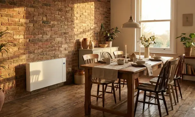 Chauffage moderne en pierre stéatite sur un mur de briques, réchauffant une salle à manger rustique avec une table en bois dressée.