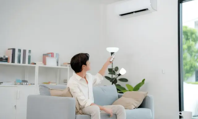 Un homme règle sa télécommande clim Toshiba en mode chauffage depuis son canapé.
