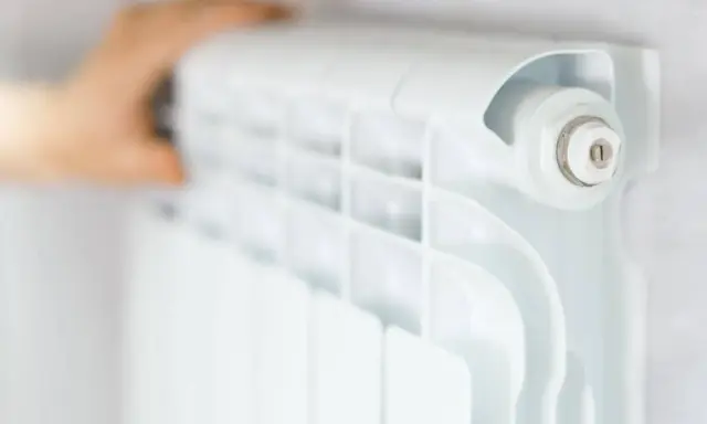 Main d'une personne ajustant un radiateur blanc, élément clé du système chauffage maison.