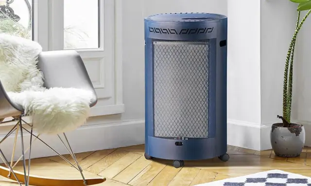 Un chauffage gaz infrarouge ou infrableu bleu, cylindrique et sur roulettes, diffuse sa chaleur dans un salon cosy, près d'un fauteuil confortable.