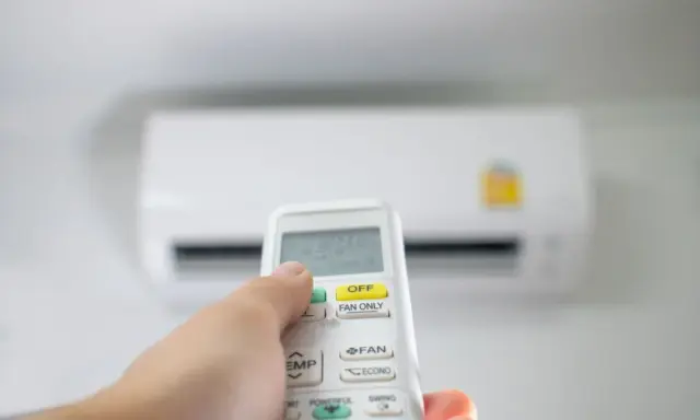 Main tenant utilise la télécommande pour régler la clim en été. La température est affichée sur l'écran.