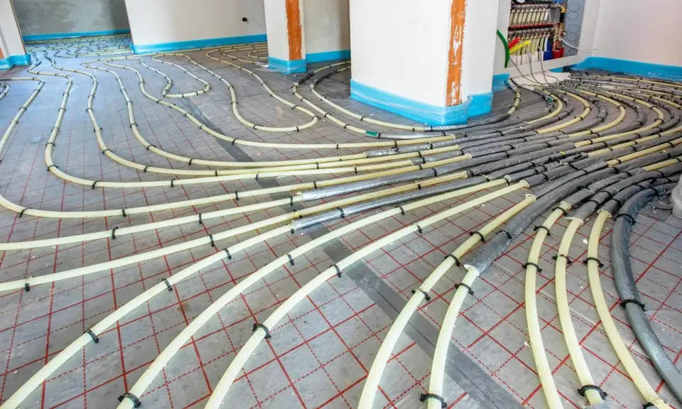 Installation de tubes pour un système de chauffage au sol. Les tuyaux jaunes sont fixés sur une grille rouge, prêts à être recouverts.