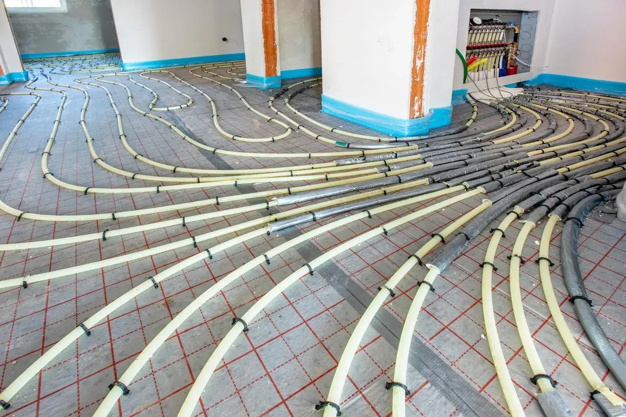 Installation de tubes pour un système de chauffage au sol. Les tuyaux jaunes sont fixés sur une grille rouge, prêts à être recouverts.
