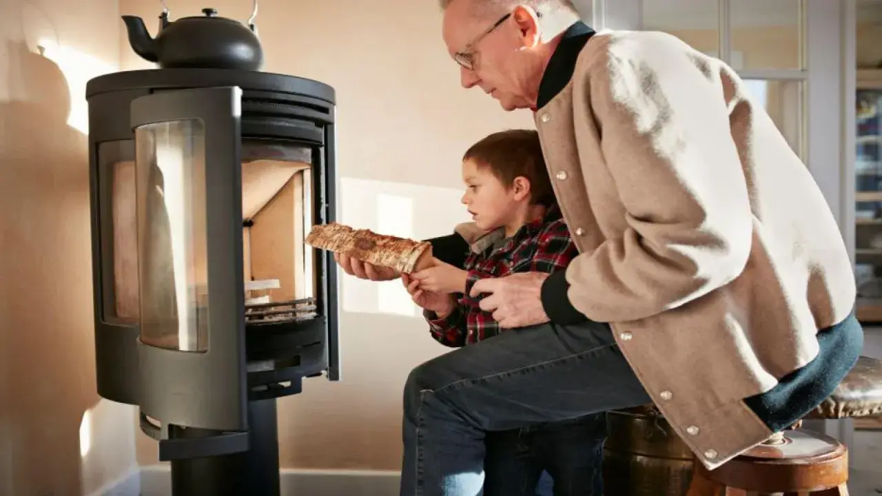 Un grand-père aide son petit-fils à charger du bois dans un poêle. Une alternative au chauffage au fioul, mais attention aux dangers du feu.