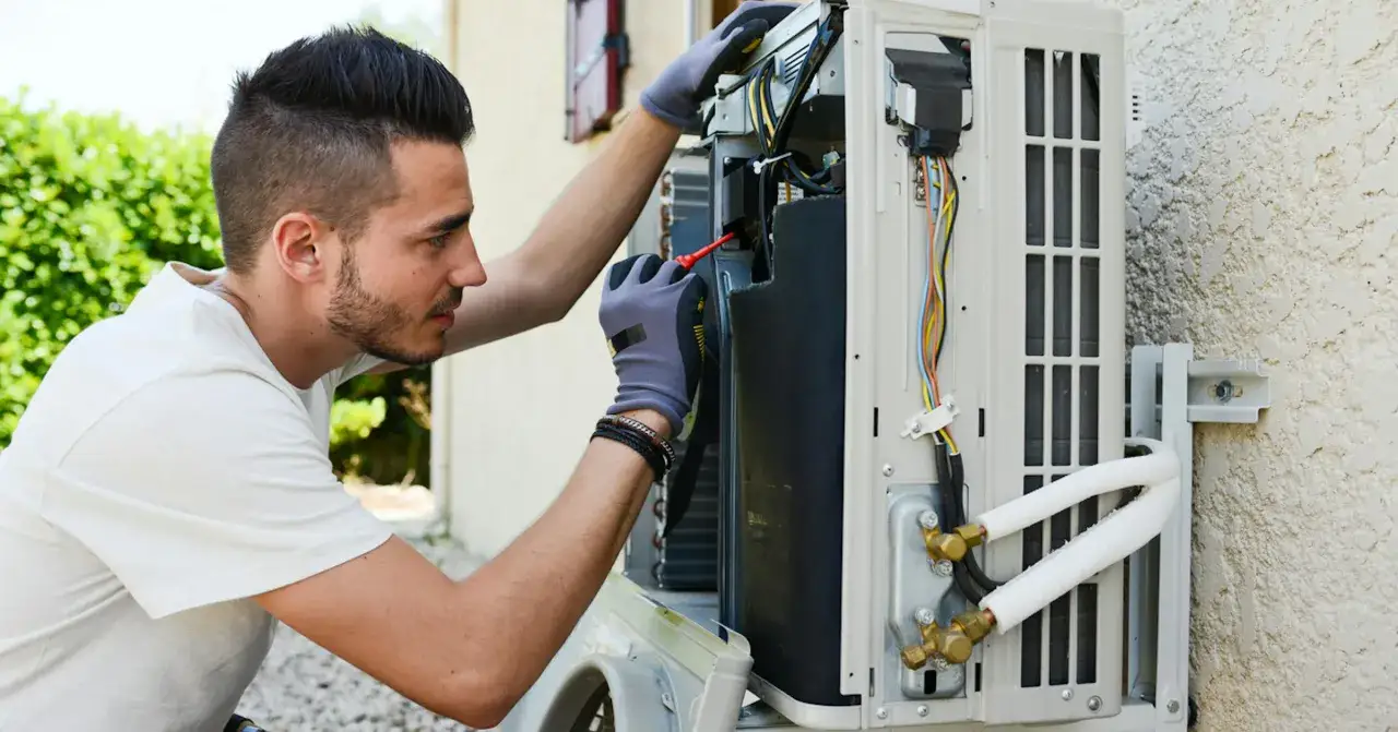 Un technicien vérifie un climatiseur extérieur. Il est concentré sur les fils et les composants. Le tarif dépannage climatisation est une préoccupation pour les propriétaires.