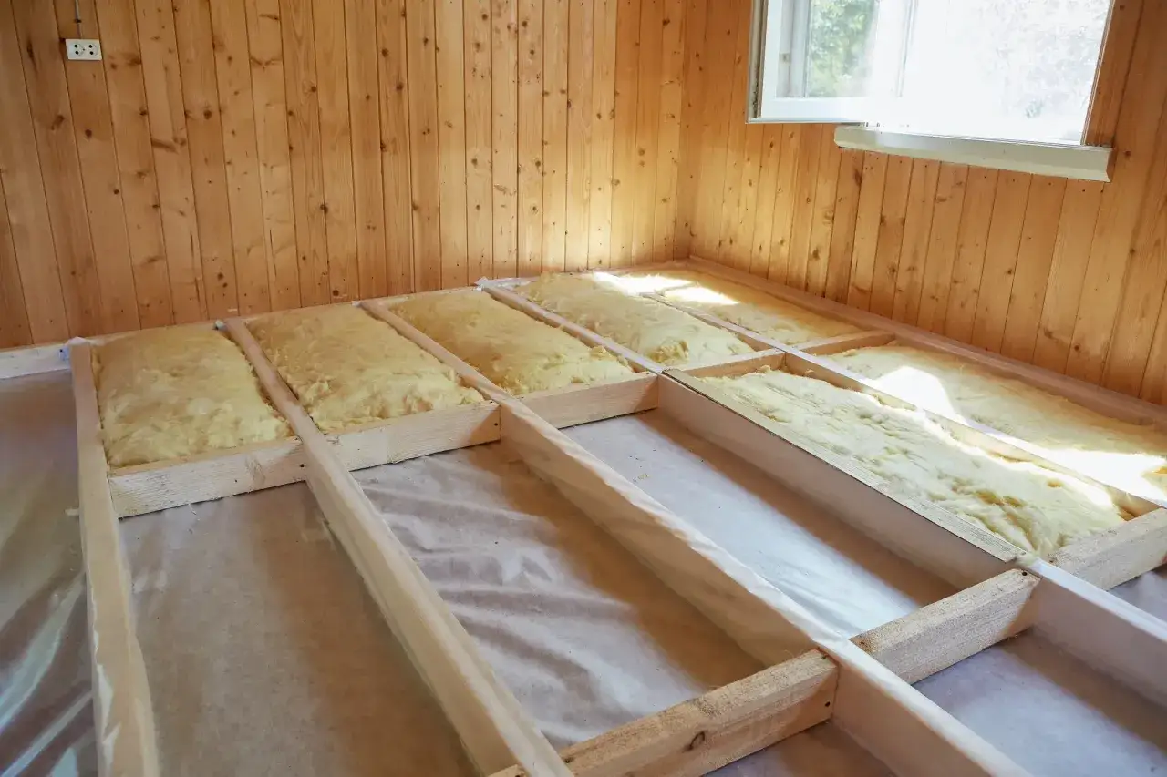 Pose de l'isolation plancher bois. Laine min&eacute;rale jaune install&eacute;e entre les solives en bois, pr&ecirc;te pour la prochaine &eacute;tape de construction.