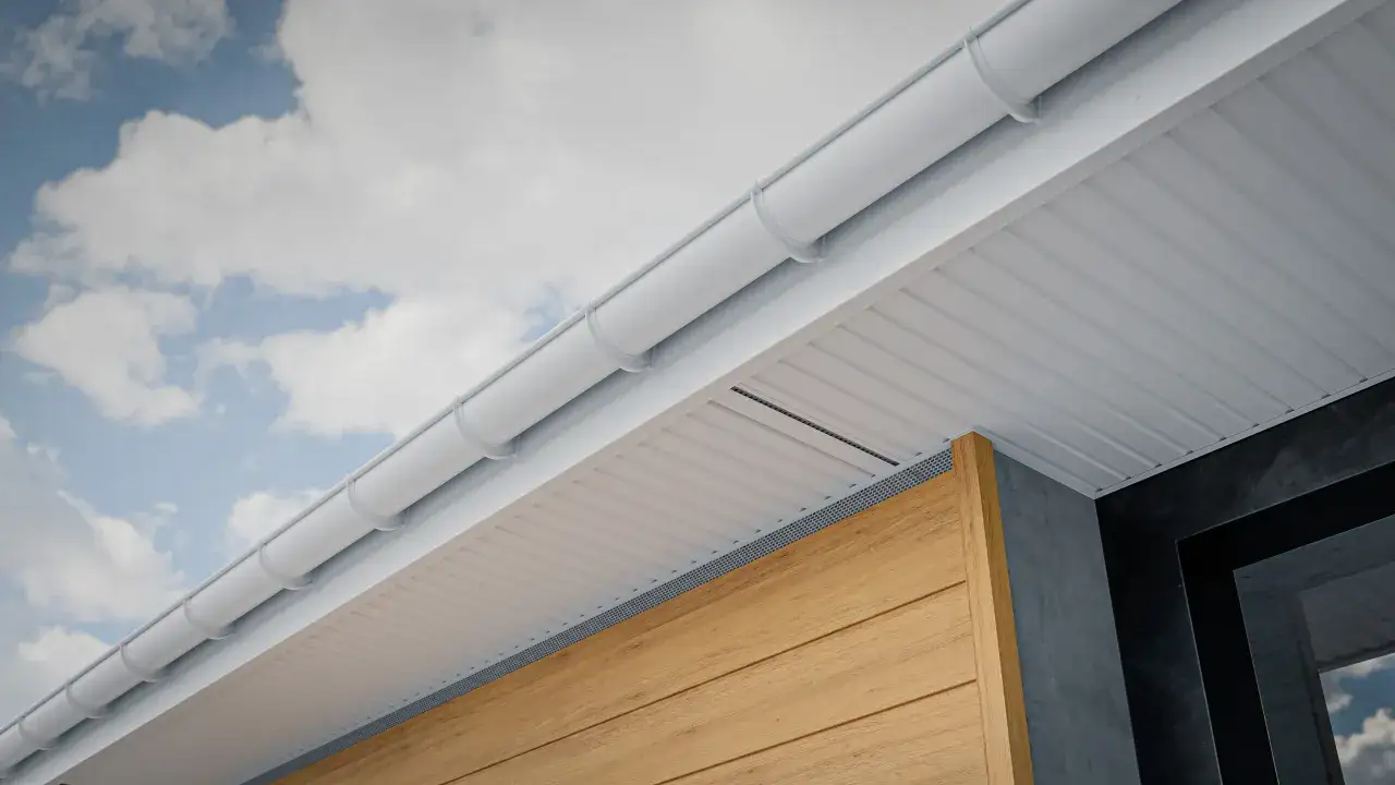 Goutti&egrave;re blanche et soffite blanc ray&eacute;, sous un ciel bleu nuageux. La toiture froide est bien visible, avec un bardage en bois clair et un mur sombre.