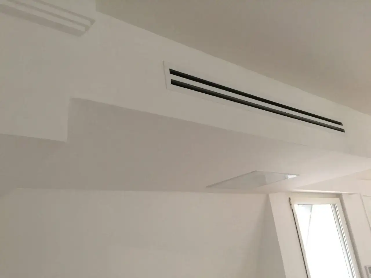 Ventilation discr&egrave;te int&eacute;gr&eacute;e au plafond blanc, assurant un confort thermique invisible.