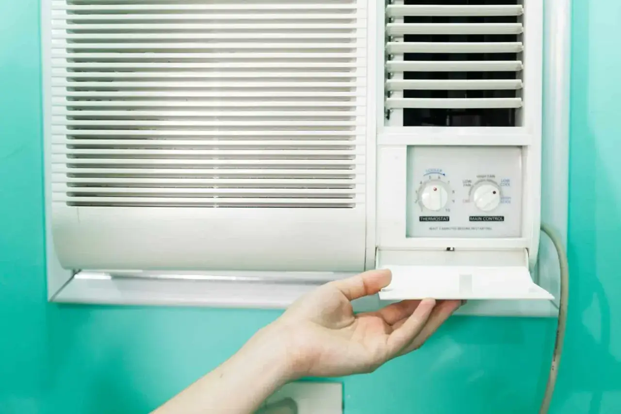 Clim 3.5 kW : quelle surface refroidir ? Une main ouvre le compartiment d'un climatiseur mural blanc.