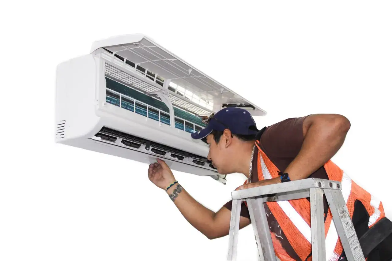 Technicien sur une &eacute;chelle, v&eacute;rifiant un climatiseur mural. Il s'assure que le syst&egrave;me est pr&ecirc;t pour une recharge clim mobile.