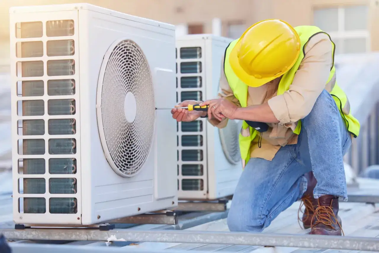 Technicien en jaune, ajustant un climatiseur ext&eacute;rieur. Il s'assure que le clim souffle chaud et froid pour le confort de tous.