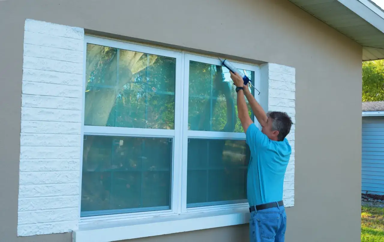 Un homme applique du mastic pour isoler fenetre froid. Il am&eacute;liore l'&eacute;tanch&eacute;it&eacute; de la maison.