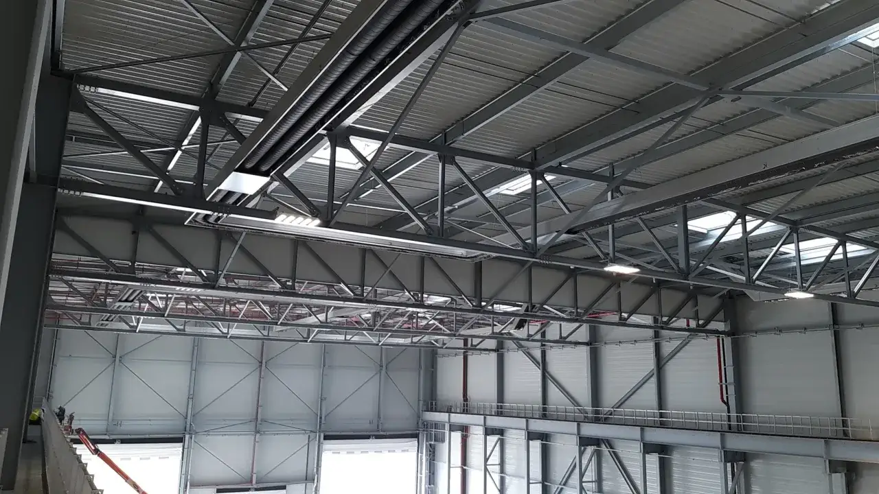 Vue d'un grand entrep&ocirc;t avec une structure m&eacute;tallique complexe. Des conduits et des lumi&egrave;res sont visibles, sugg&eacute;rant un syst&egrave;me d'aerotherme chauffage.