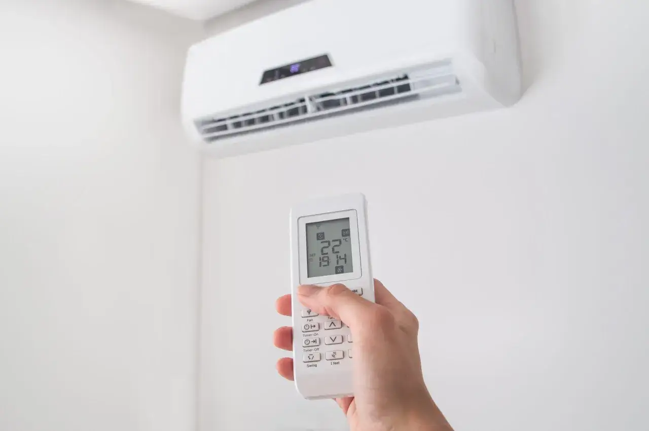 Main d'une personne tenant une télécommande d'air conditionné, affichant 22°C. Le symbole du flocon de neige, souvent présent sur ces appareils, indique le mode froid.